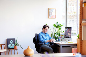 Smiling man using smartphone in office - obrazy, fototapety, plakaty
