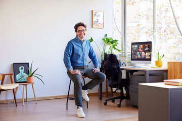 Cheerful businessman sitting on stool in light office