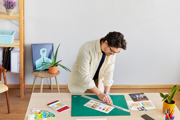 Male artist cutting pictures at table in creative studio