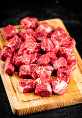Raw pieces of beef on a wooden cutting board.
