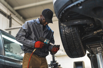 Low-angle shot of a black mechanic repairing a car wheel with an impact wrench. Repair shop concept. High quality photo
