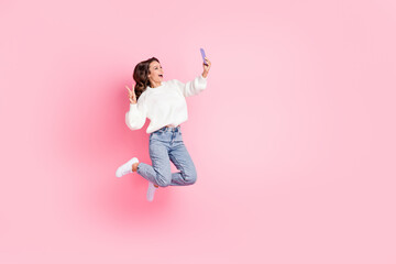 Full length photo of friendly woman dressed pullover jumping showing v-sign device empty space...