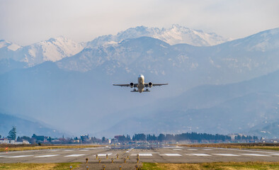 Passenger airplane takes off from airport runway with mountains in background.