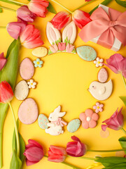 Sweets, pastry, gingerbread cookies for Easter table. Easter eggs, rabbit and tender simple flowers and tulips on yellow background, spring seasonal holiday wreath, banner for your site, flyer, coupon