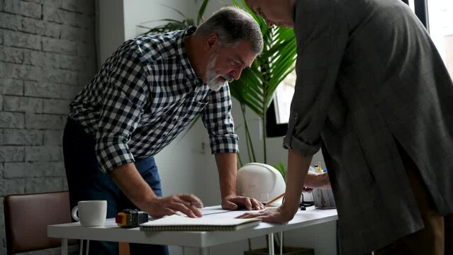 Two cropped architects discussing floor plan at table in office. Design of the house. Engineer. Tools for drawing. Creating a drawing.