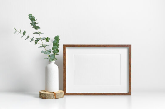 Horizontal picture frame mockup in white minimalistic scandinavian interior with fresh eucalyptus decorations.