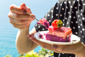 Strawberry cake in a plate in female hands against the backdrop sea. Decorating torts with whole berries. - obrazy, fototapety, plakaty