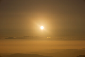 Dramatic sunset on a foggy winter day, shot above the clouds. Mountain range covered with clouds.