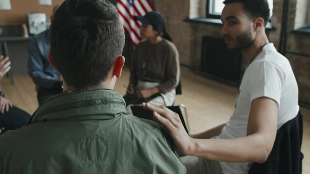 Slow motion of sympathetic young man carefully listening to and comforting his new friend during group therapy session