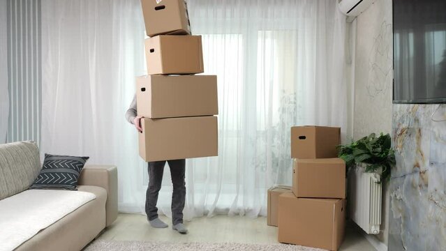 Man carries stack of boxes in arms and falls down on floor in new apartment. Black-haired guy helps with moving into new house and tries to hold boxes