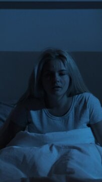Nightmare stress. Night terror. Sleep disorder. Scared disturbed woman waking up from bad dream in bed in dark bedroom. Vertical video.