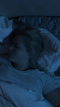 Night terror. Bad dream. Nightmare anxiety. Disturbed woman tossing turning sleeping alone in bed late in dark blue light. Vertical video.