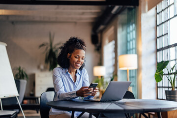Smiling businesswoman using a mobile phone while working online.