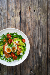 Salmon salad - smoked salmon, hard boiled eggs, avocado and leafy greens on wooden table
