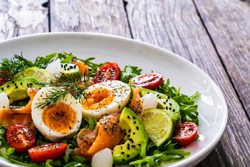 Salmon salad - smoked salmon, hard boiled eggs, avocado and leafy greens on wooden table
