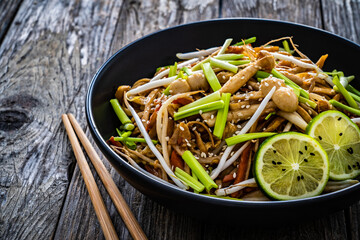 Asian food - Chow Mein noodles, stir fried vegetables, soy sauce and shimeji mushrooms on wooden table
