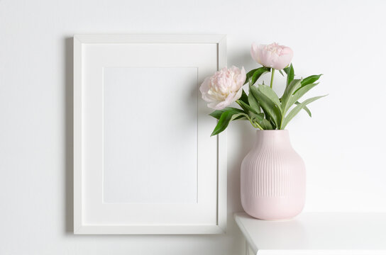 Frame mockup on white wall with pink peony flowers in vase, mockup for artwork presentation