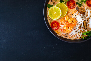Tom Yum - Thai soup with prawns, shiitake mushrooms and noodles on wooden table

