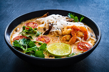 Tom Yum - Thai soup with prawns, shiitake mushrooms and noodles on wooden table
