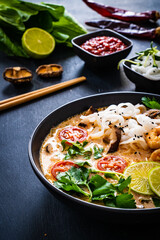 Tom Yum - Thai soup with prawns, shiitake mushrooms and noodles on wooden table
