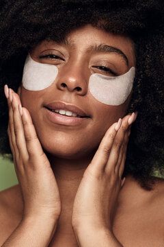 Crop young black lady with eye patches touching face during skincare treatment