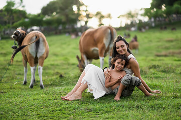 Fototapeta premium Happy mom and son hugging in the meadow, among the cows.