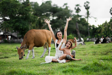 Fototapeta premium Happy mom and son hugging in the meadow, among the cows.