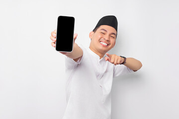 Smiling young Asian Muslim man pointing finger at display mobile phone screen isolated on white...