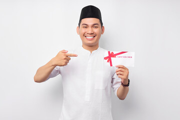 Smiling young Asian Muslim man pointing finger at gift certificate coupon voucher isolated on white...