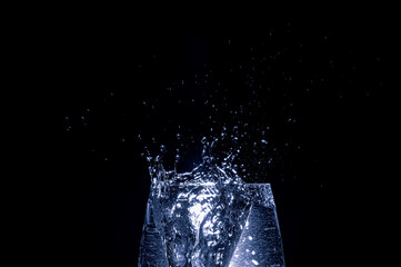 Eiswürfel fällt ins Wasserglas, dunkler Hintergrund