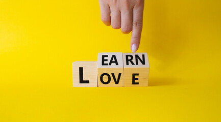 Learn and Love symbol. Businessman hand points at turned wooden cubes with words Love and Learn. Beautiful yellow background. Lifestyle and Learn and Love concept. Copy space.