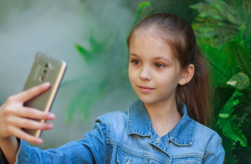 Portrait of a beautiful girl close-up outdoors, the child takes a selfie using a smartphone, a beautiful look and a smile.
