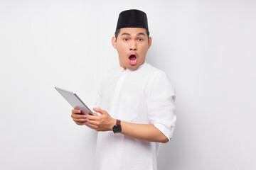 Surprised young Asian Muslim man using digital tablet and reacting to online news isolated on white background. People religious Islam lifestyle concept. celebration Ramadan and ied Mubarak