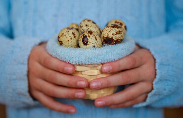 Basket with quail eggs in the hands of a child. Blue background, Easter concept. Religious holiday of Easter.
