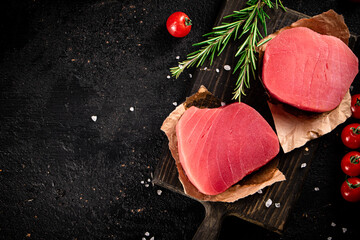 Raw tuna on a cutting board with tomatoes and rosemary. 