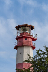 Fototapeta na wymiar Gelendzhik. Modern lighthouse on thick cape. Multifaceted red and white column of lighthouse tower is 50 meters high against blue sky with white clouds. Close-up.