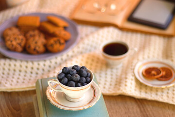 Obraz na płótnie Canvas Plate of cookies, cup of tea, fresh blueberries, dry oranges, stack of books, reading glasses and tablet on the table. Hygge at home. Selective focus.