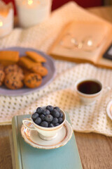 Plate of cookies, cup of tea, fresh blueberries, dry oranges, stack of books, reading glasses and tablet on the table. Hygge at home. Selective focus.