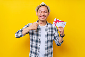 Smiling handsome Asian ethnicity young man 20s wearing casual clothes hat pointing finger at gift certificate coupon voucher card for store isolated on yellow background. People lifestyle concept