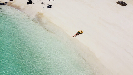 Aerial view of woman relaxing on the tropical sandy beach. Top wide shot of a girl lying with big summer hat, sunbathing. A lot of copy space. Tourism. Travel. © neonshot