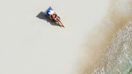 Aerial photo of woman relaxing on the tropical beach, reading book and sunbathing. Tourism. Traveler.