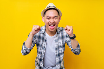 excited fun Young handsome ethnic Asian man 20s wearing casual clothes hat making winner gesture celebrating clenching fists saying yes isolated on yellow background. People lifestyle concept