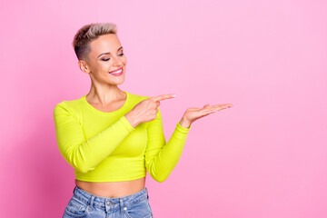 Portrait of pretty positive girl toothy smile look indicate finger arm hold empty space isolated on pink color background