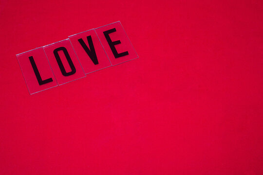 Palabra LOVE escrita con letras negras en mayuscula sobre un fondo rojo por el d&iacute;a de los enamorados.