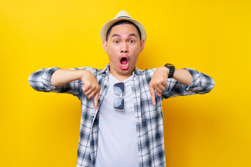 Shocked Young handsome ethnic Asian man 20s wearing casual clothes hat standing pointing index fingers down on mock up copy space isolated on yellow background. People lifestyle concept