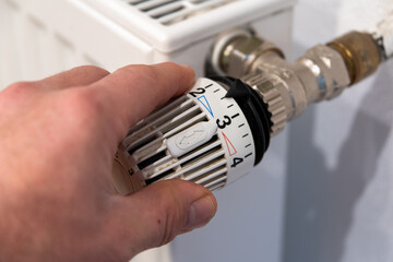 Male hand turns a radiator thermostat