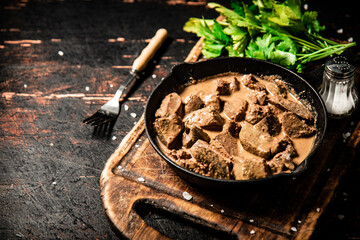 Liver in a frying pan on a cutting board with parsley and spices. 