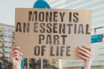 The phrase "Money is an essential part of life " is on a banner in men's hands with blurred background. Economy. Finance. Salary. Financial. Profit. Boss. Buy. Richness. Got. Economic. Exchange. Save