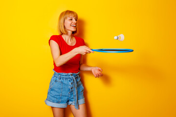 Woman having fun playing badminton on yellow background