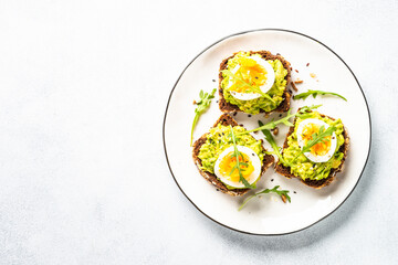 Open sandwich. Whole grain bread with avocado and boiled eggs. Top view on white kitchen table.